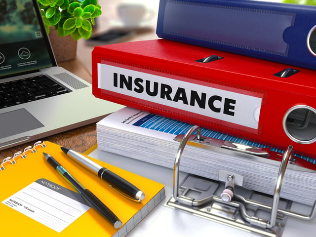 Red Ring Binder with Inscription Insurance on Background of Working Table with Office Supplies, Laptop, Reports. Toned Illustration. Business Concept on Blurred Background.